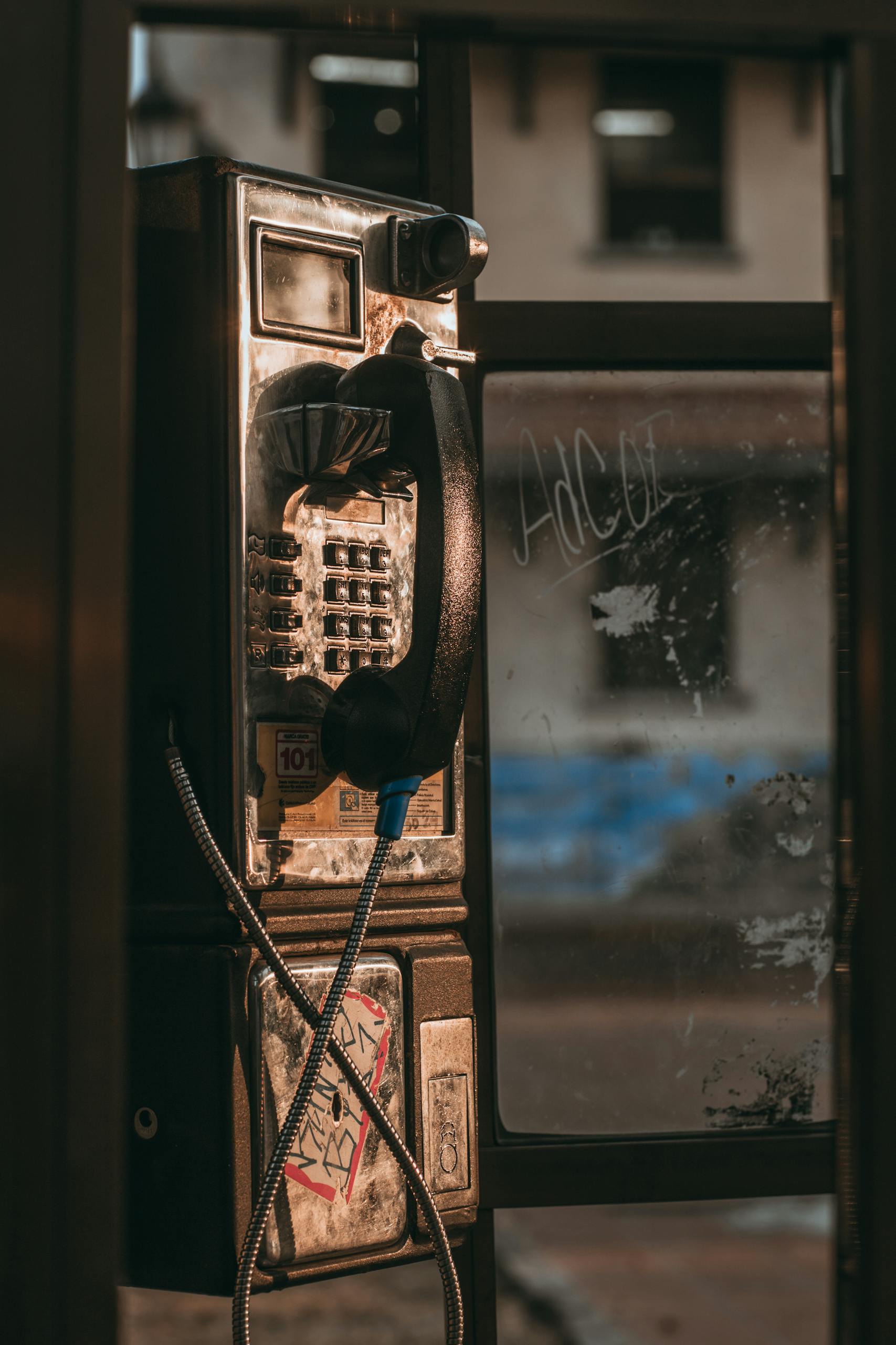 A vintage telephone booth with a rusty exterior on an urban street.